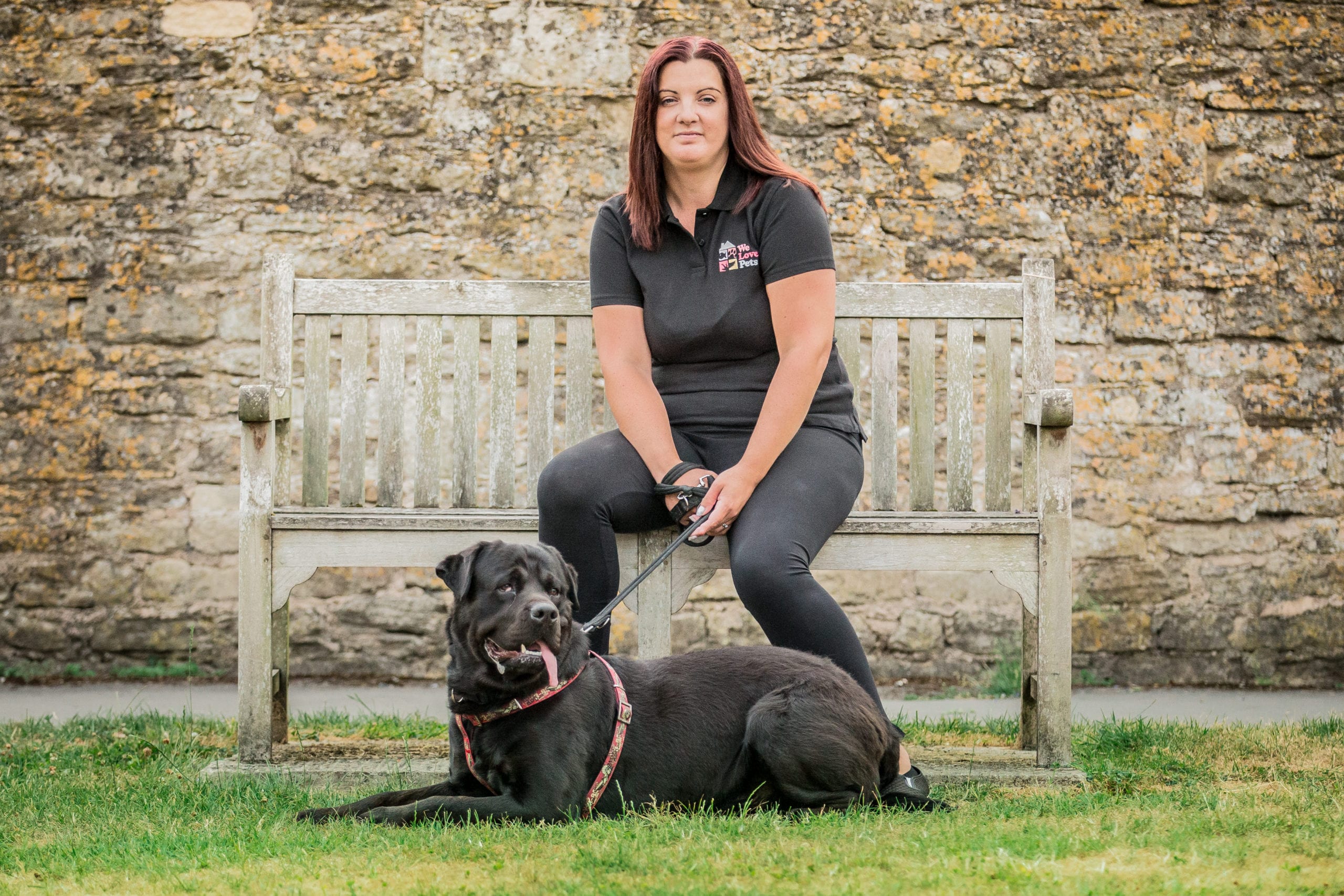 Jo from We Love Pets Trowbridge sitting on a bench with a dog laying in front of her