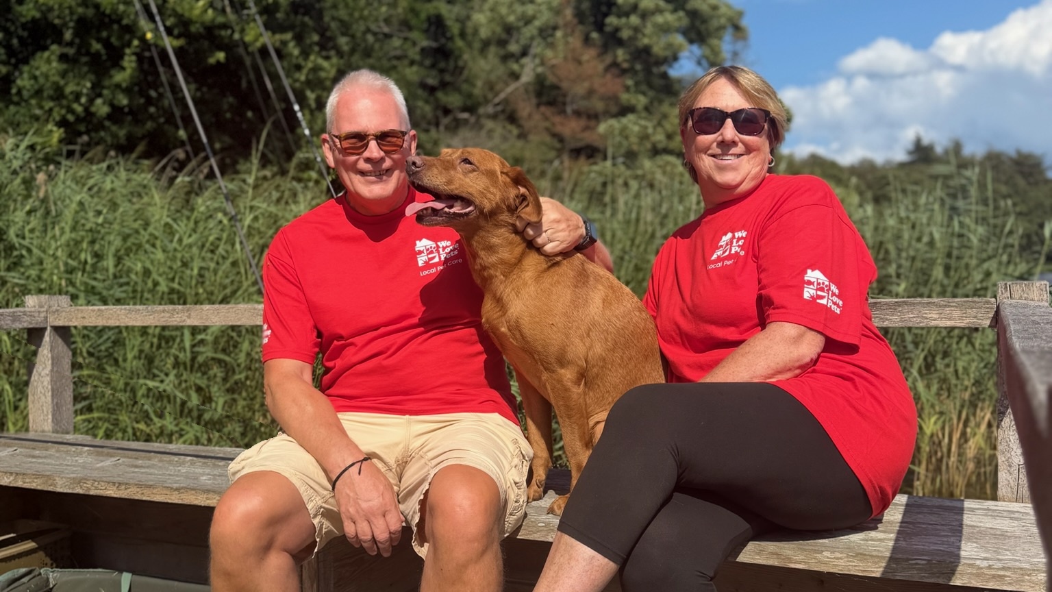 Two We Love Pets franchisees sitting with a dog by a lake